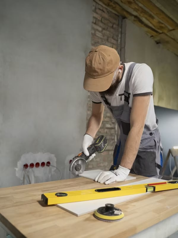 Man using a power tool on a wooden work surface, with a level and tile, in a home improvement setting reflecting Bison Works' construction expertise.