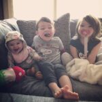 Three children sitting on a couch, smiling and playing, showcasing a joyful family moment.