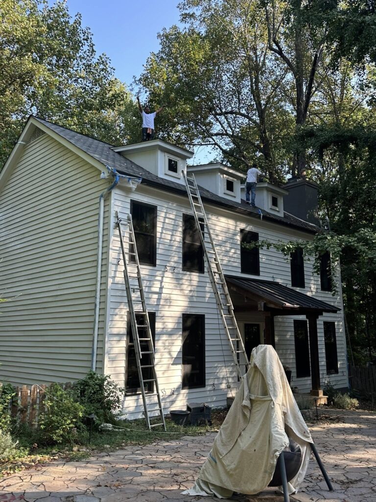 Roofing technicians working on a residential home, with ladders positioned against the house, showcasing the installation process and commitment to quality roofing services by BisonWorks.