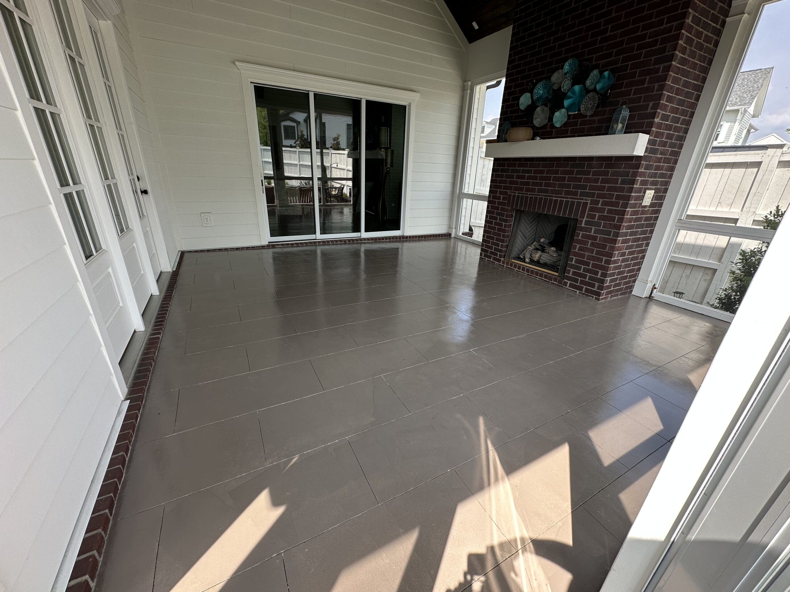 Spacious covered patio with polished flooring, brick fireplace, and large glass doors, showcasing a modern outdoor living space.