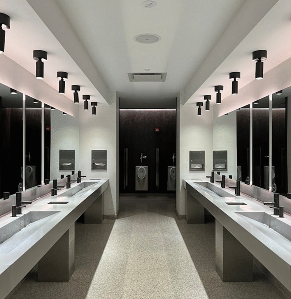 Modern commercial bathroom interior with sleek double vanity sinks, contemporary lighting fixtures, and mirrors, showcasing a clean and stylish design for home improvement inspiration.