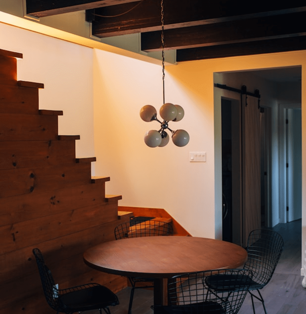 Modern dining area featuring wooden staircase, round table with black wire chairs, and contemporary pendant light fixture, showcasing Bison Works' home improvement craftsmanship.