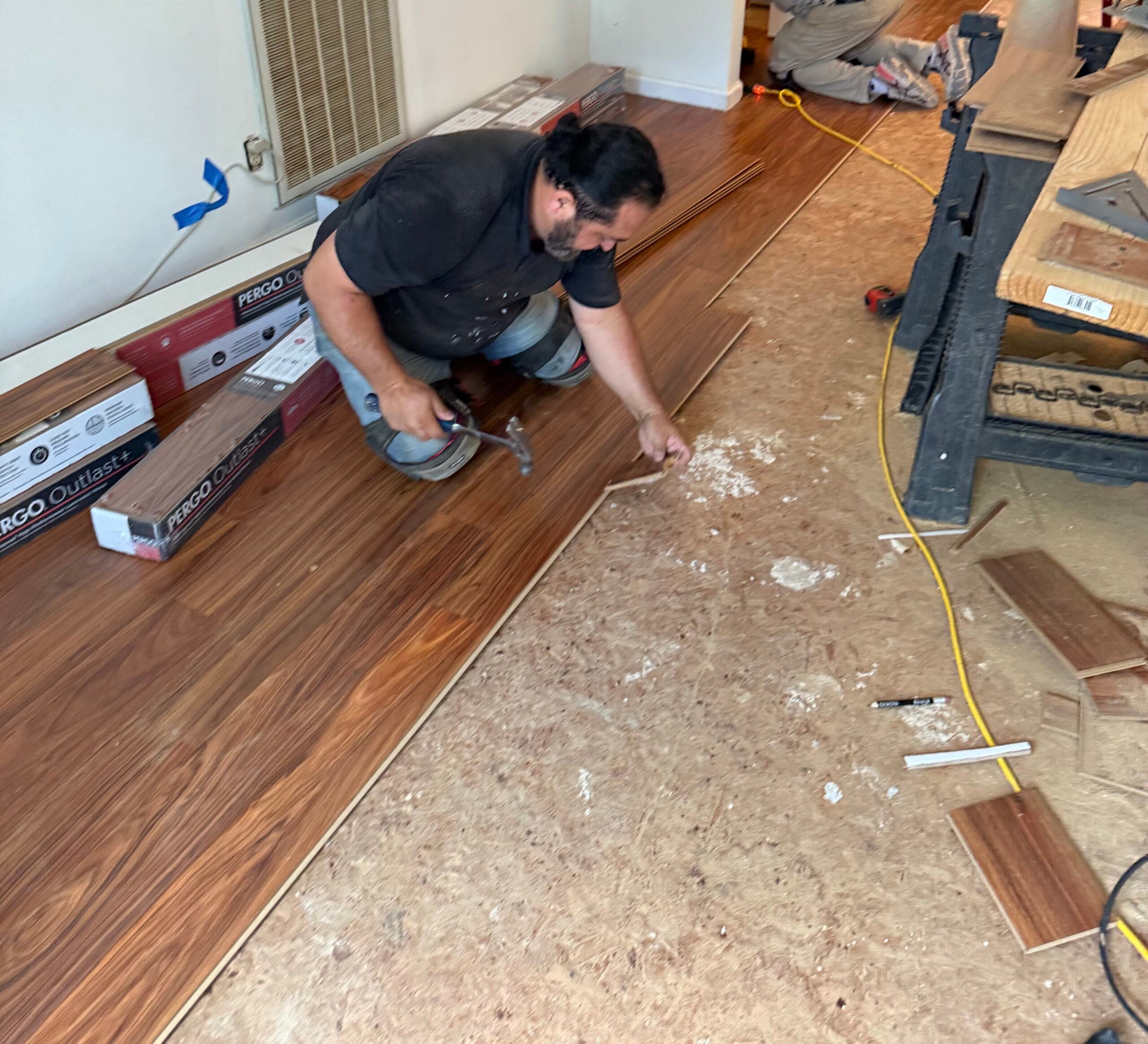 Man installing laminate flooring with tools in a residential setting, showcasing expert craftsmanship and attention to detail for home improvement.