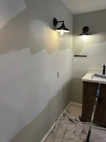 Partially painted bathroom wall with two wall sconces and a sink.